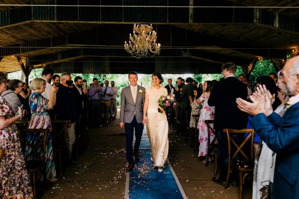 father of the bride walks his daughter down the aisle surrounded by guests