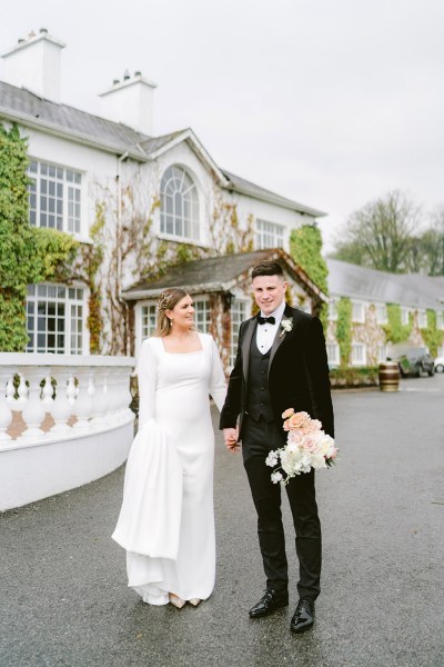 bride and groom walk holding hands outside of venue entrance