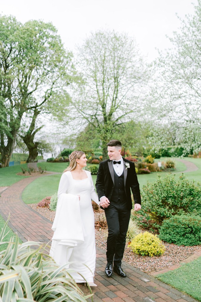 bride and groom walk through the gardens holding hands