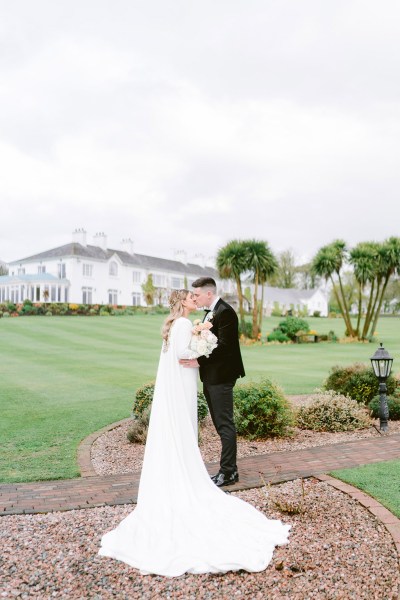 bride and groom with venue in background kiss