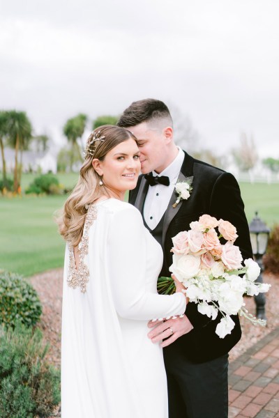 bride and groom close kiss on the cheek bride looks to camera holding bouquet