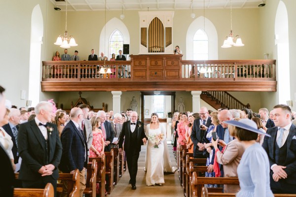 father of the bride walks his daughter down the aisle surrounded by guests either side