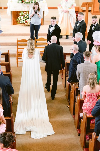 father of the bride walks his daughter down the aisle surrounded by guests either side