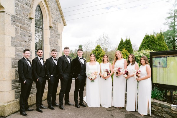 bridesmaids bride and groom and groomsmen on either side stand in courtyard together