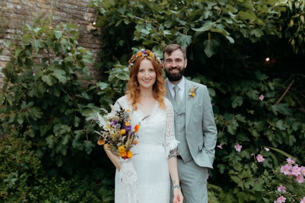 bride and groom standing in the garden she holds bouquet