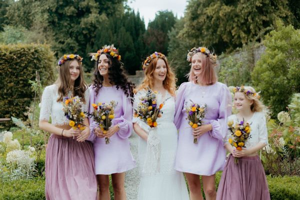 bride in the middle of bridesmaids wearing lilac dresses holding bouquet smiling