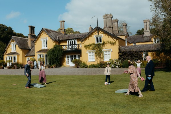 wedding venue in background to guests enjoying the sun on grass setting