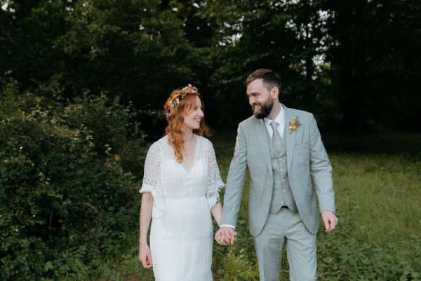 bride and groom walk on the pathway to forest together holding hands they look at each other