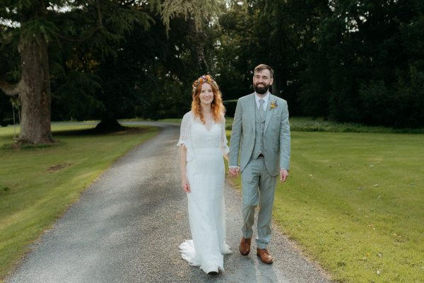 bride and groom walk on the pathway to forest together holding hands