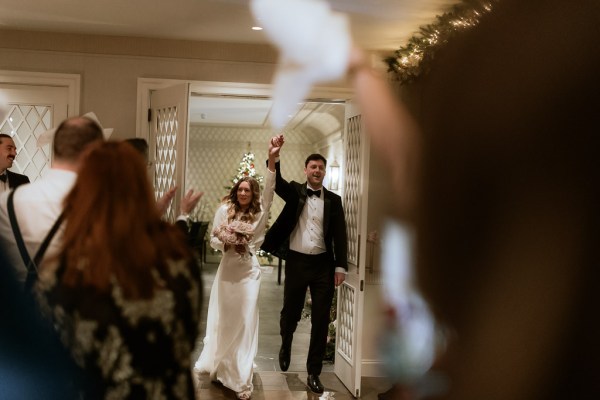 bride and groom walk into ballroom all smiles guests waiting for them