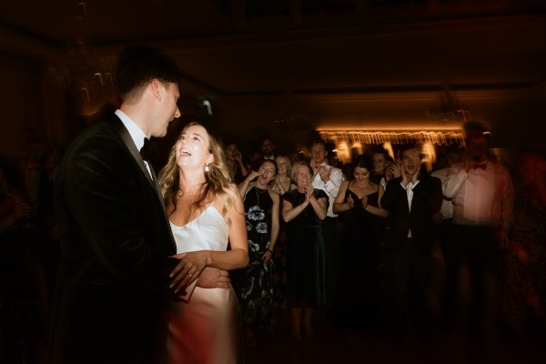 dark image of bride and groom smiling at each other guests in background