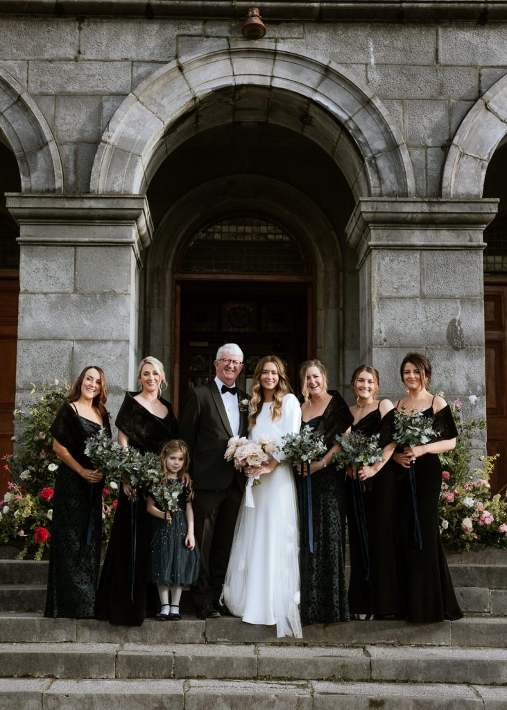 bride and groom outside church chapel entrance bridesmaids wearing black on either side archway