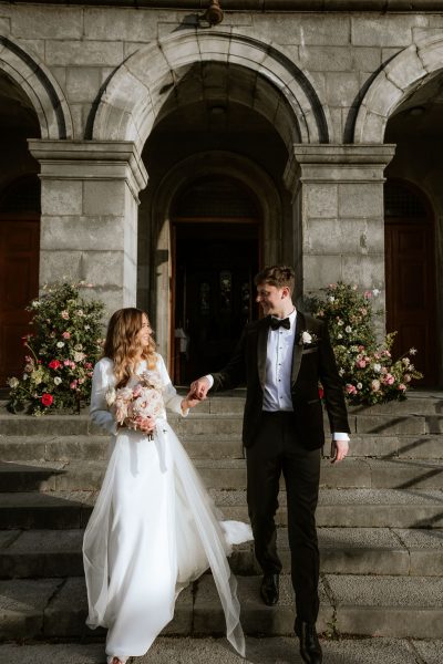 bride and groom stand in front of steps pillars in background