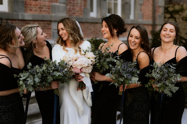 bride and her bridesmaids wearing black dresses holding bouquets smile