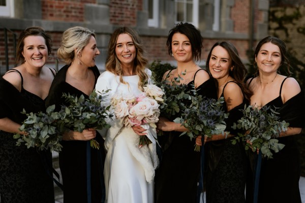 bride and her bridesmaids wearing black dresses holding bouquets smile