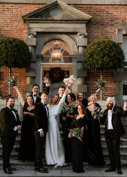 groom bride bridesmaids and groomsmen all pose on wedding venue steps