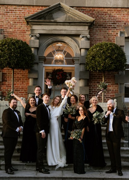 groom bride bridesmaids and groomsmen all pose on wedding venue steps