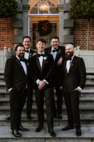 groom and his groomsmen smiling together on wedding venue steps