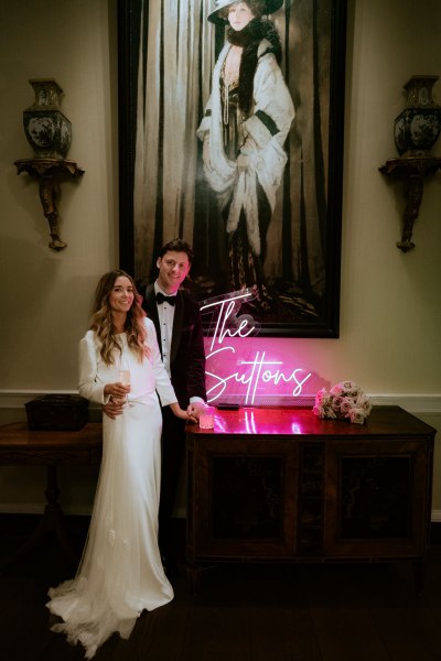 The Suttons pink sign and bride and groom smiling they smile/laugh