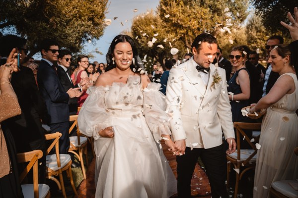 bride and groom exit wedding ceremony hand in hand confetti is being thrown over couple