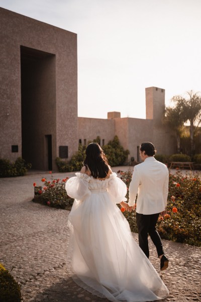 bride and groom walking towards venue from behind hand in hand