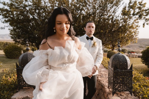 bride walks ahead of groom trees in background