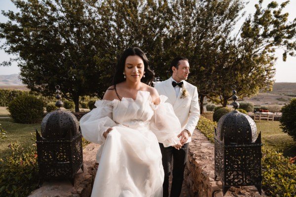 bride walks ahead of groom trees in background