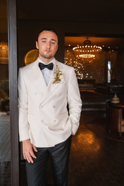 groom in bowtie leans against doorframe to venue