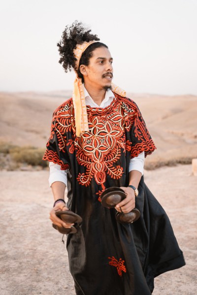 man in traditional outfit and headband walks in the desert