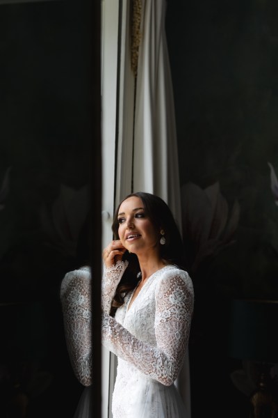 bride puts on her earrings looking out from window