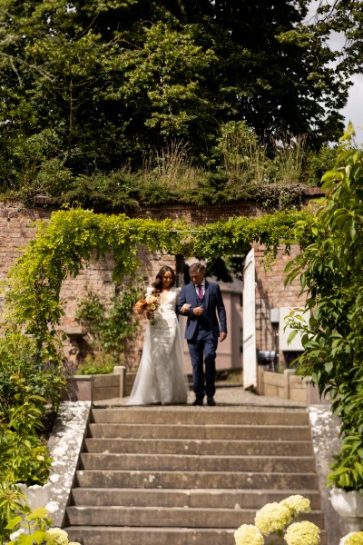 father of the bride walks down the aisle down the steps towards ceremony