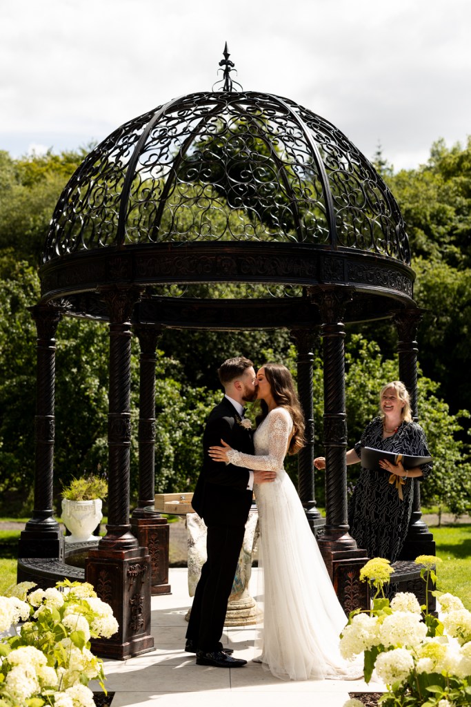 bride groom hut in background celebrant giving speech they kiss