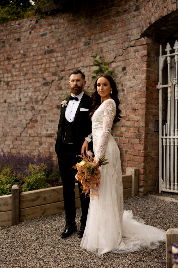 bride and groom look to the side she holds bouquet they both stand in front of gate