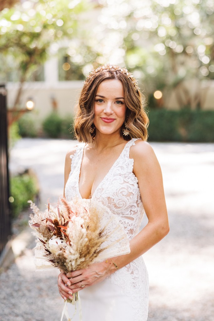 bride on her own holding bouquet smiles on pathway she looks ahead holding bouquet