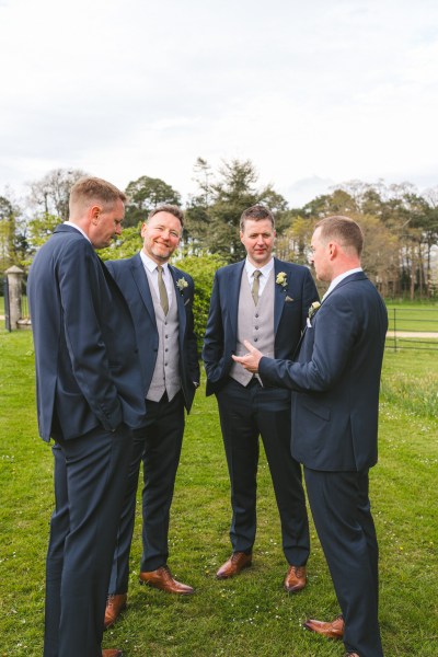 groom and groomsmen chat on the green grass