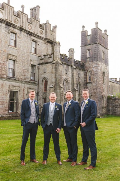 groom and groomsmen stand on the green grass