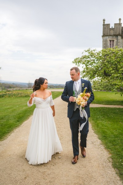 bride and groom walk the pathway to venue he holds her bouquet