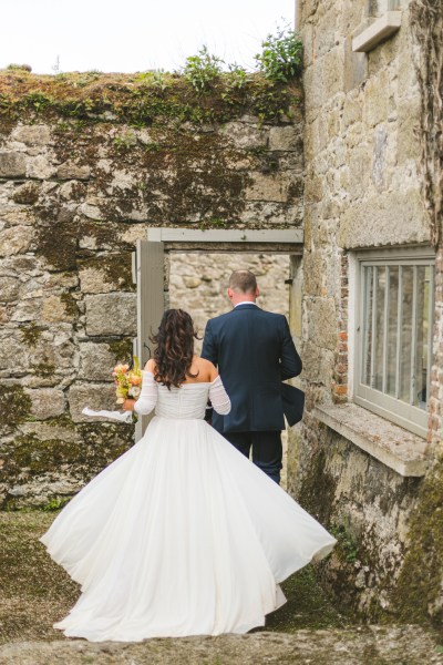 bride and groom from behind walk through the garden together