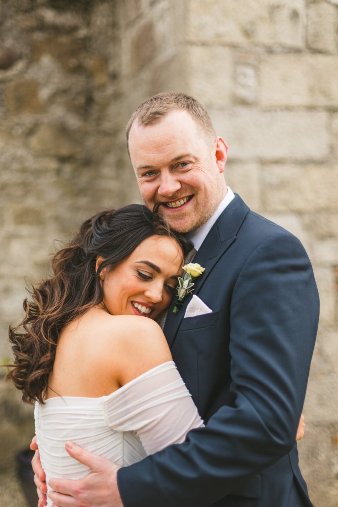 bride and groom stand in the courtyard together and smile looking at each other and hugging