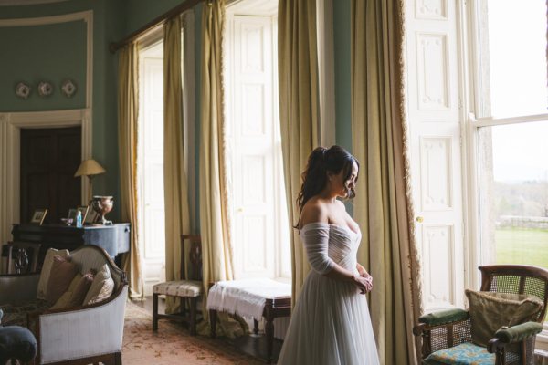 bride stands in room facing window