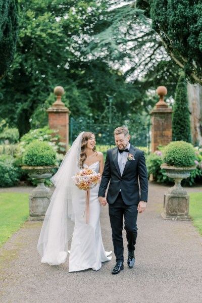 Bride and groom walk holding hands in garden during first look