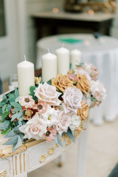 Orange, pink and cream flower display with cream column candles on a table