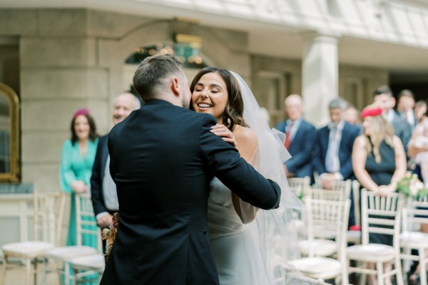 Bride and groom embrace at the top of an alter as guests look on