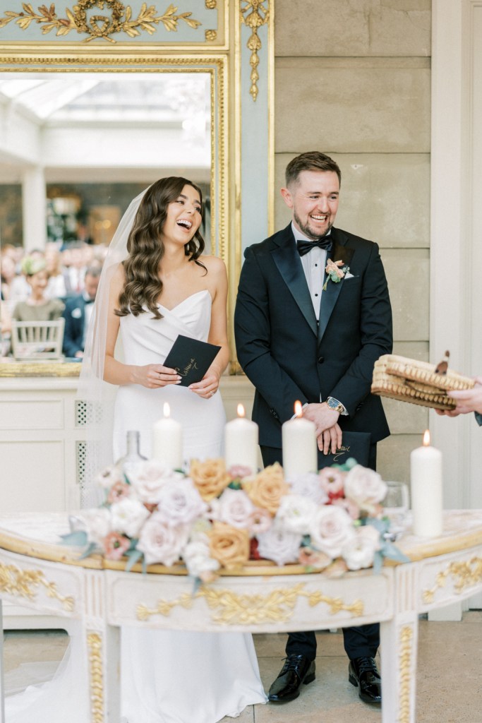 Bride and groom laugh in front of ceremony table wit flowers and candles