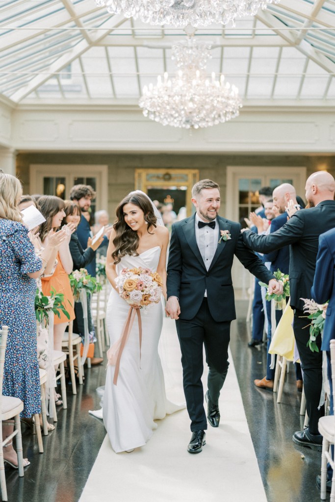 Bride and groom walk down the aisle greeting guests 