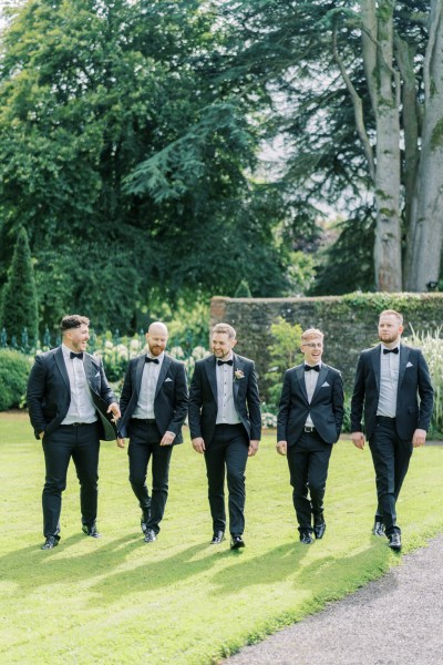 Groom with his groomsmen walking across a lawn in a garden