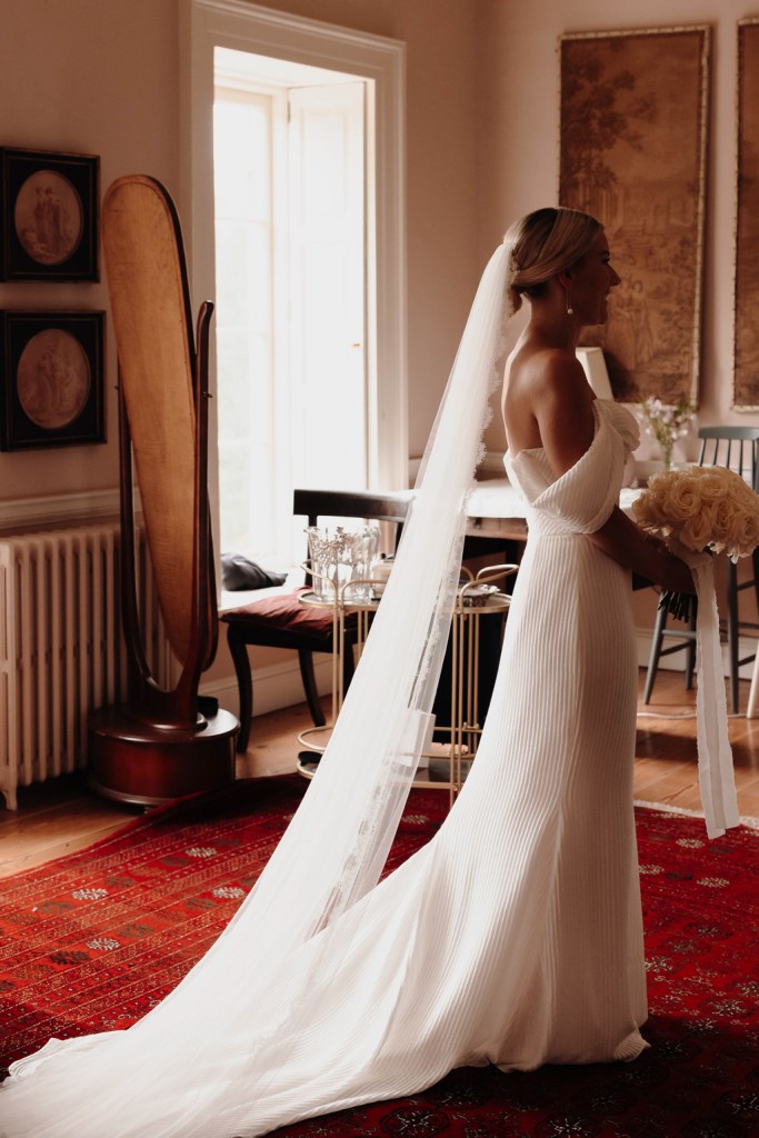 bride stands in room long veil on ground red carpet