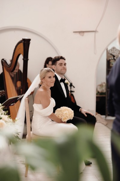 bride and groom sitting at alter she holds bouquet harp in background