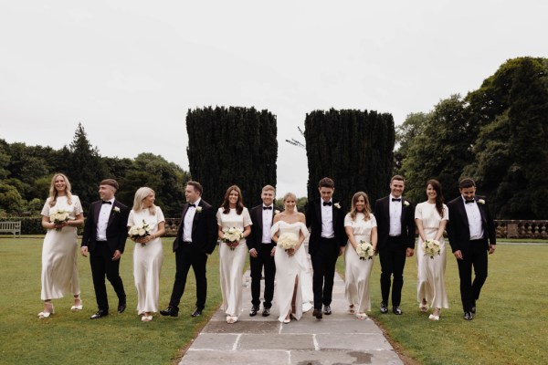 bride groom groomsmen bridesmaids all walking in a line in garden