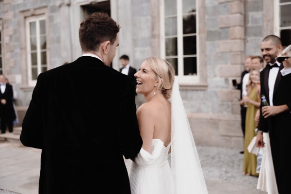 bride and groom walking together smiling in courtyard wearing veil